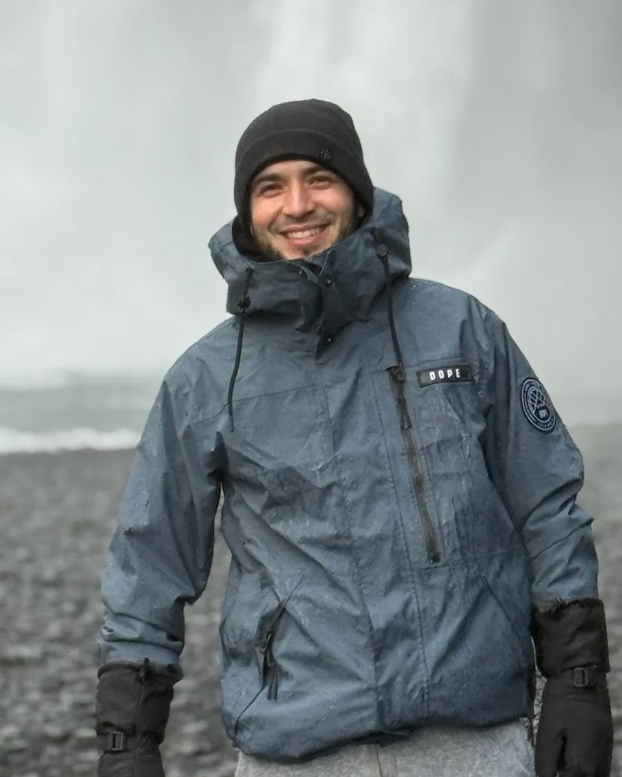 Andrés Montero in front of a waterfall on a black-sand beach in Iceland